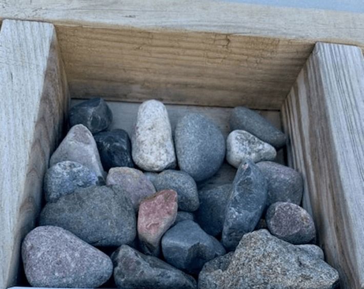 Wooden box filled with assorted smooth stones and pebbles in gray, black, and pink tones
