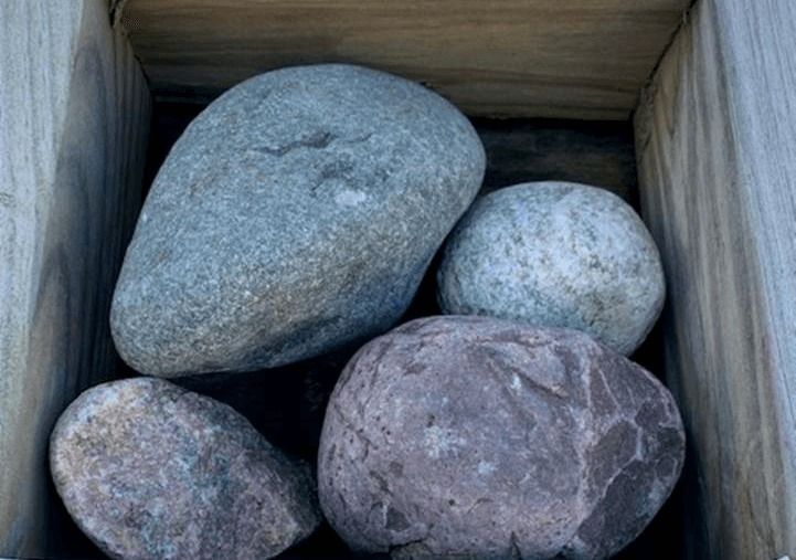 Four smooth gray and brown rocks in a wooden crate