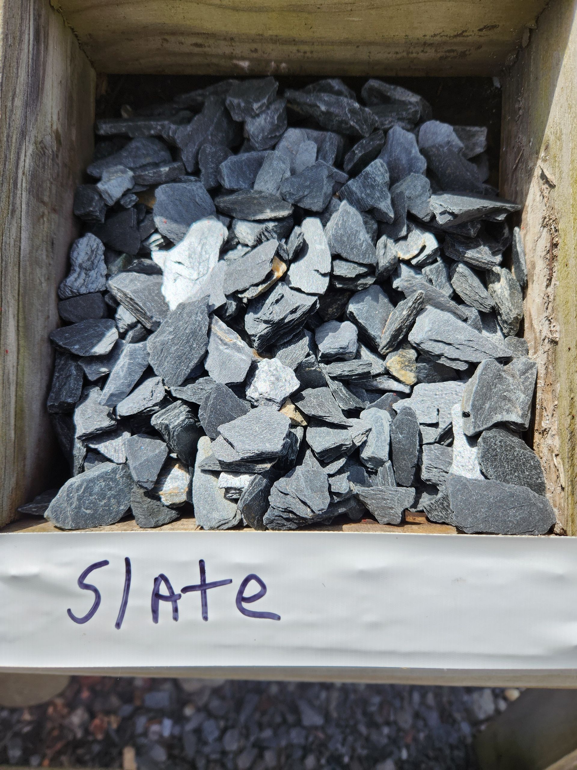 Box of small dark rocks labeled “Slate” on a shelf.
