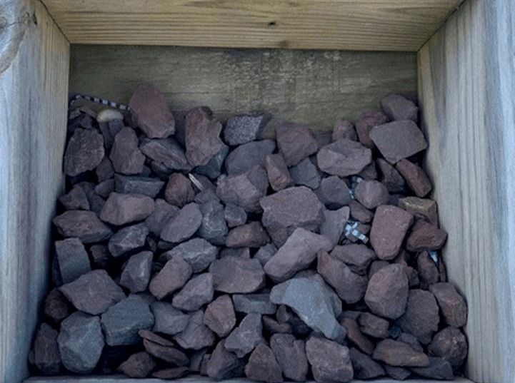 A wooden crate filled with dark purple rocks or gravel.