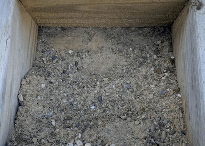 Wooden box filled with gray gravel and soil fragments