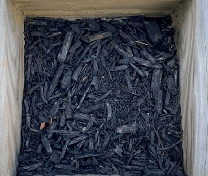 Top-down view of a wooden box filled with dark charcoal pieces and ash