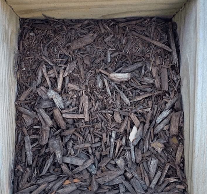 Top view of a wooden box filled with brown wood chips or mulch