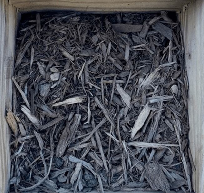 Top-down view of a wooden crate filled with gray wood chips or mulch
