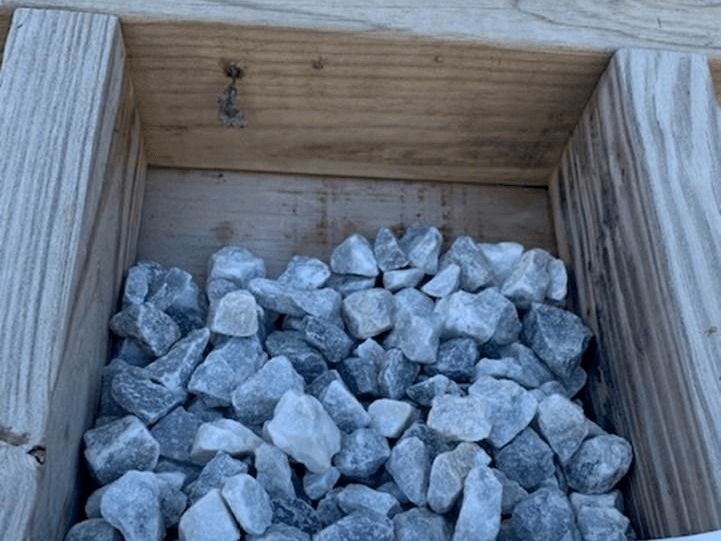 Gray rocks in a wooden box, with stacked lumber visible on the sides.