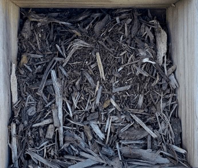 Wooden box filled with gray shredded bark or wood chips