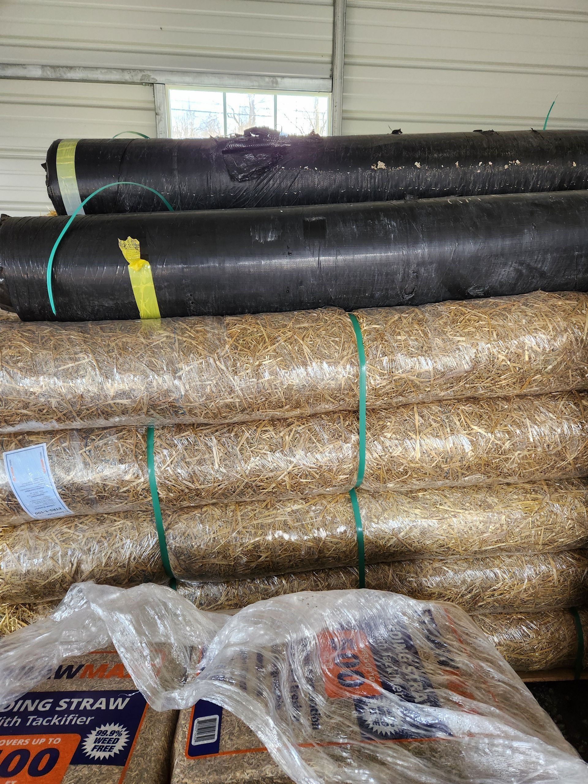 Stacks of rolled artificial turf in black and tan, bundled with straps in a warehouse.