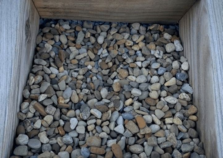 Wooden crate filled with small smooth pebbles in gray, tan, and white shades.