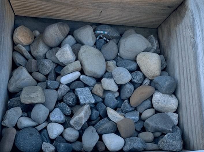 A wooden crate filled with assorted gray and tan rocks.