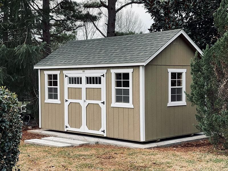Beige backyard storage shed with white trim and double doors on a gravel pad