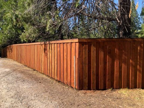 Long brown wooden fence along a gravel road beside trees and blue sky