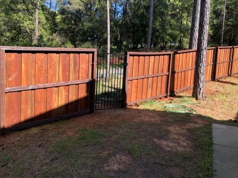 Wooden fence gate open in a yard, with grass and trees behind it.