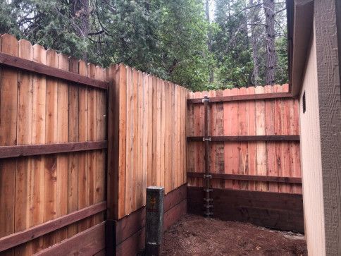 Wooden privacy fence and narrow side yard beside a house, with tall trees in the background.