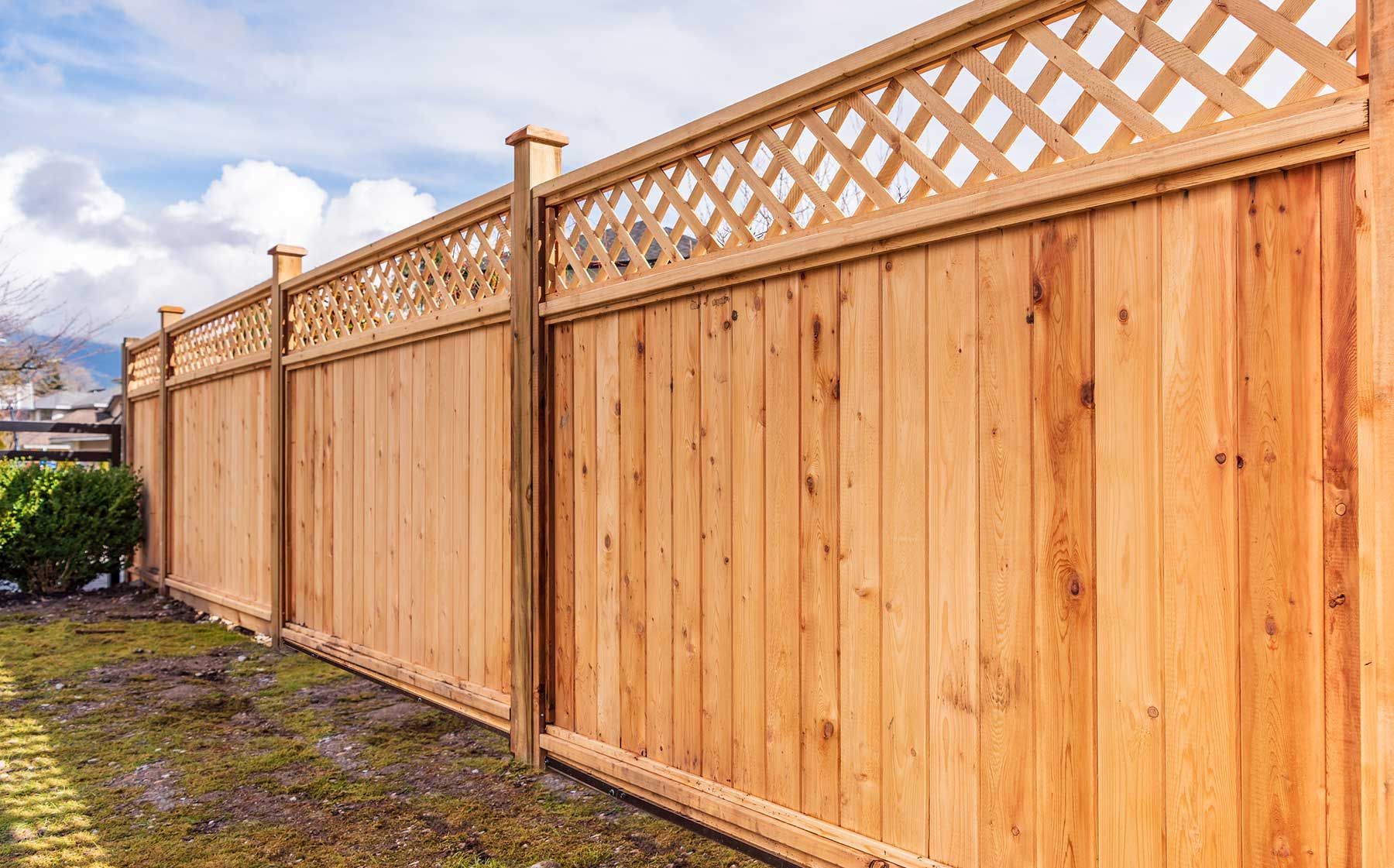 Long wooden privacy fence with lattice top along a gravel path under a cloudy sky