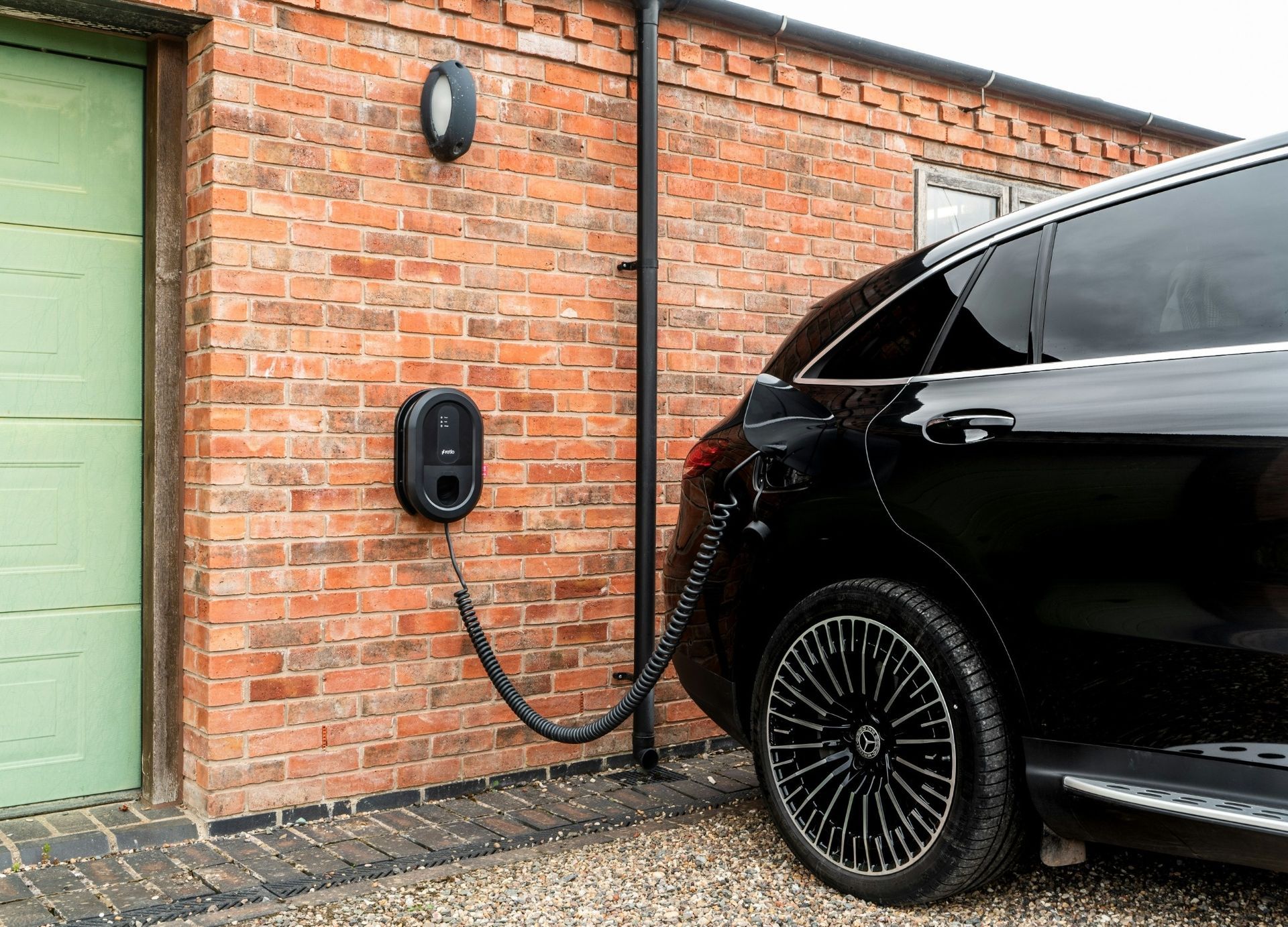 Black electric car charging beside a brick garage with a wall-mounted charger.