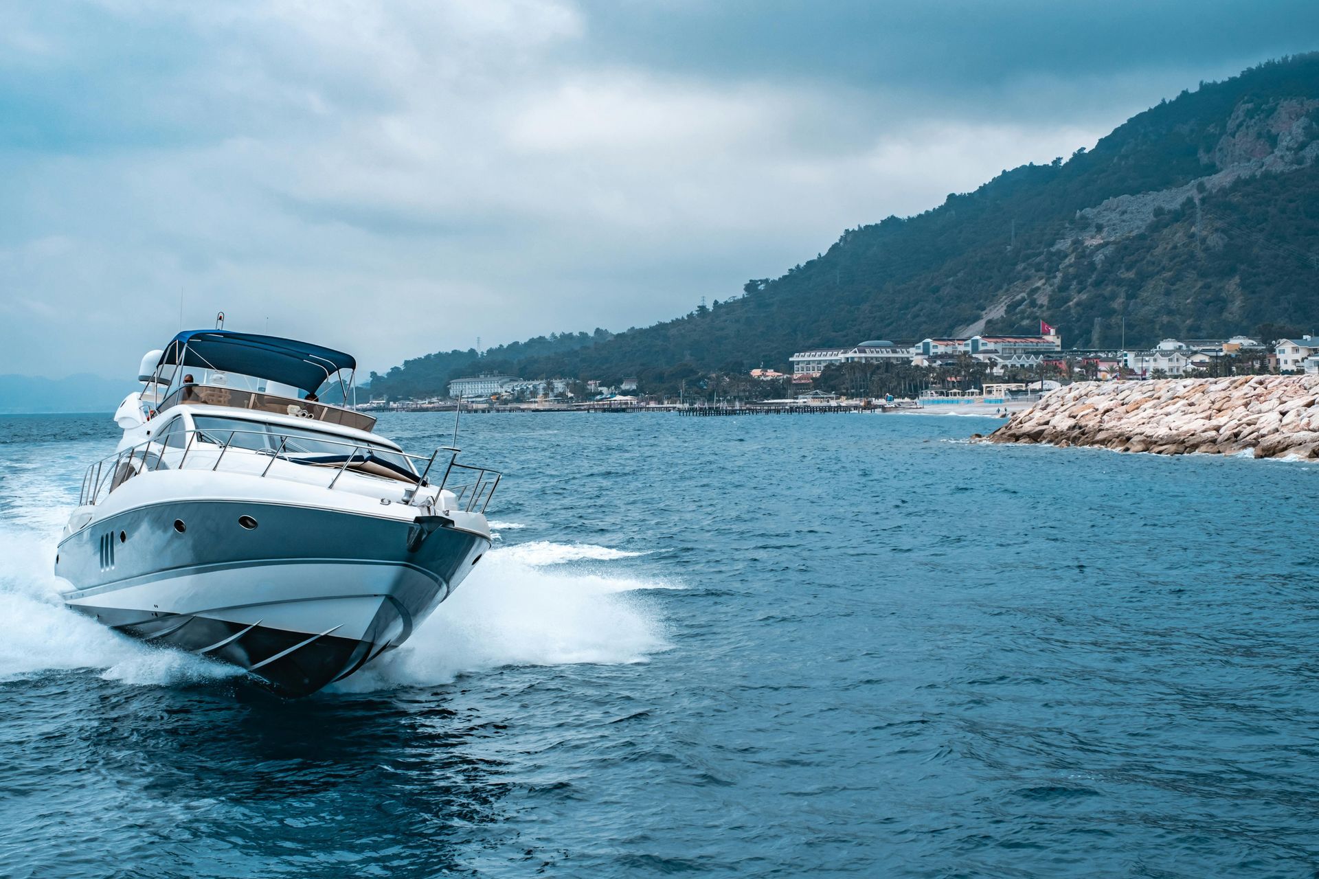 White speedboat speeding across blue water near a mountainous coastline under a cloudy sky