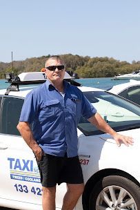 A Man in a Blue Shirt is Standing Next to a White Taxi  — Tweed Heads Coolangatta Taxi Service In Coolangatta, QLD