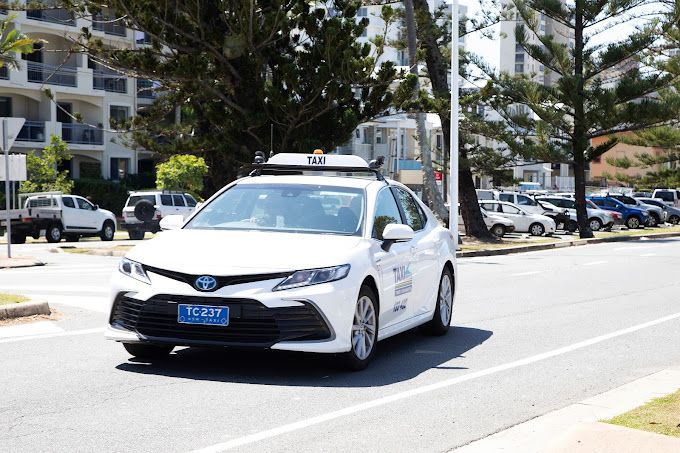 A white car is driving down a city street. — Tweed Heads Coolangatta Taxi Service In Tweed Heads, NSW