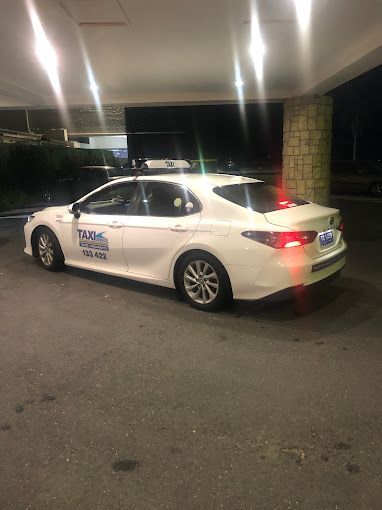 A white car is parked in a parking lot in front of a building. — Tweed Heads Coolangatta Taxi Service In Tweed Heads, NSW
