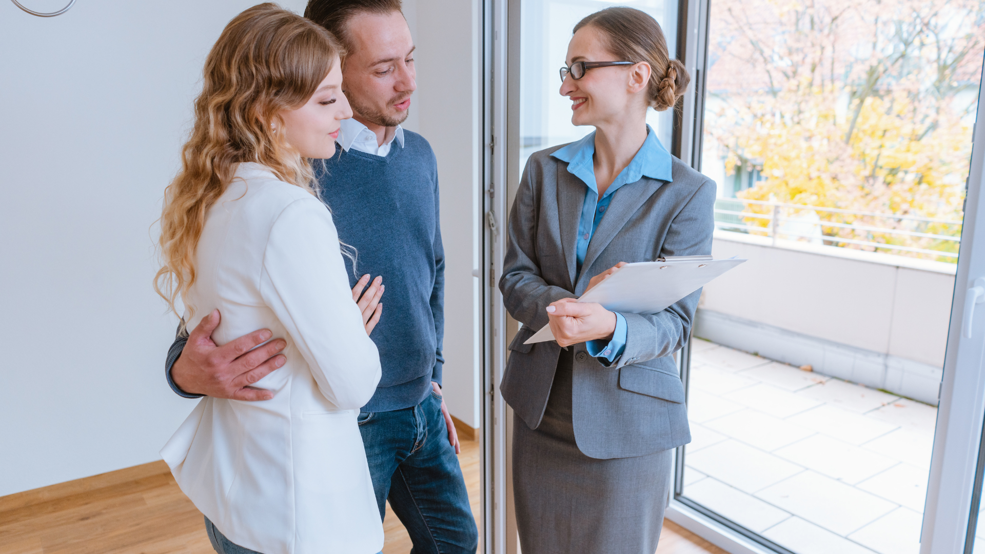 Three coworkers talking in a bright office, one holding papers and smiling.