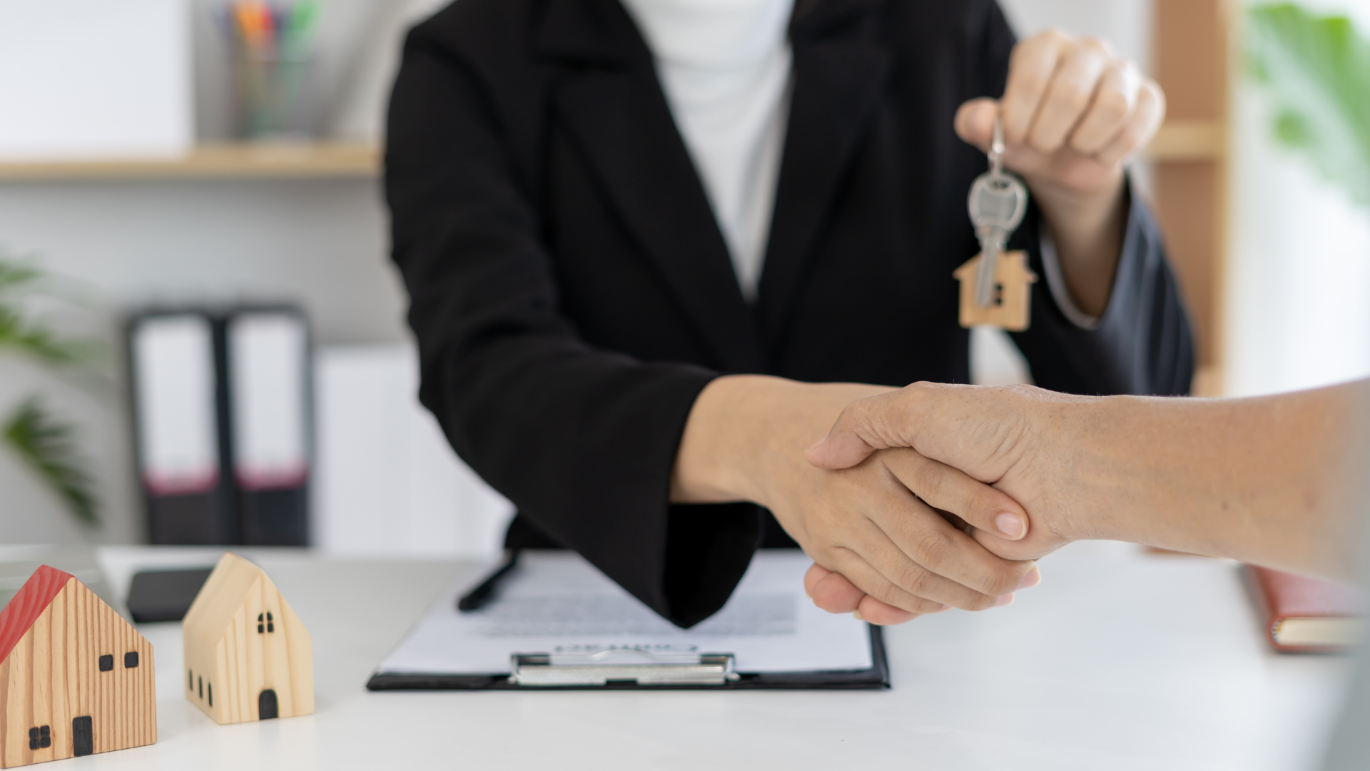 Handing over house keys during a home sale signing, with small model houses on the table