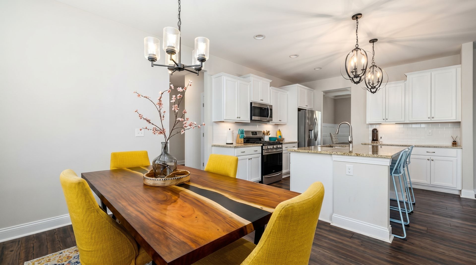 Bright kitchen-dining area with wood table, yellow chairs, white cabinets, and island under pendant lights