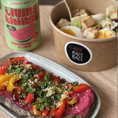 Lunch option including a redbeet hummus open toast, a salad with eggs and chicken, and a canned drink.