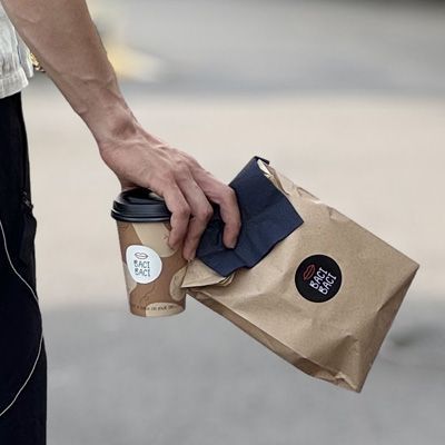 Man holding a Cafe Baci Baci branded take away coffee and paper bag.