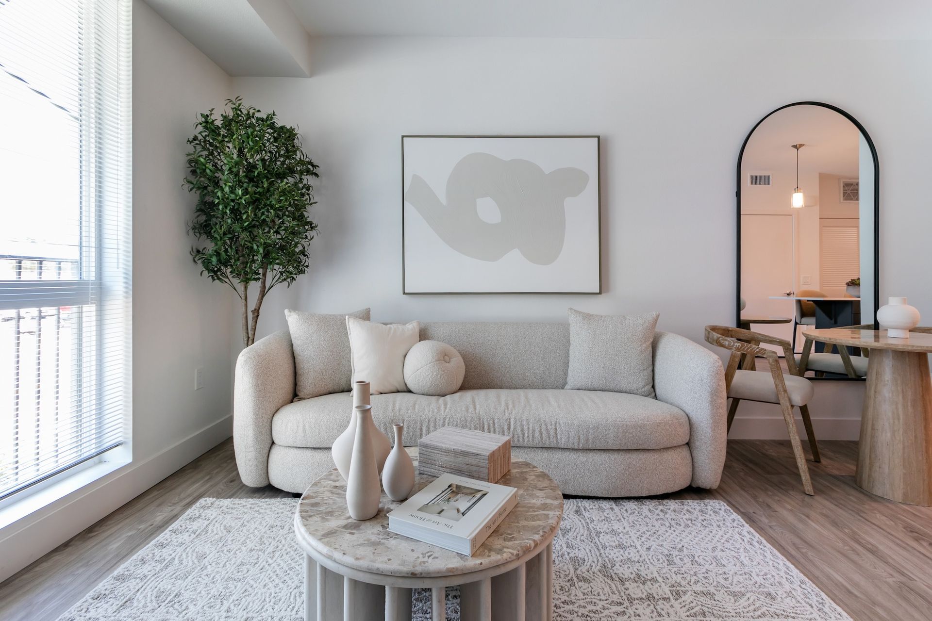 Living room with a cream-colored couch, a round coffee table, and an arched mirror.