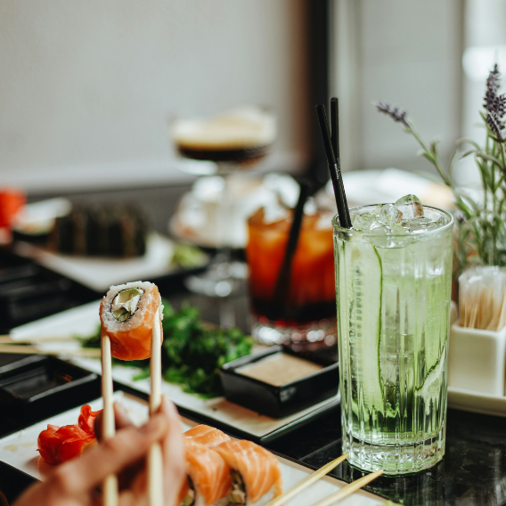 A person is eating sushi with chopsticks next to a glass of water