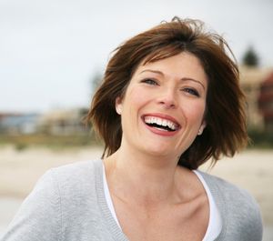 Smiling woman with short brown hair outdoors in a light gray sweater