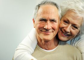 Smiling couple embracing, with the woman leaning her head on the man's shoulder.