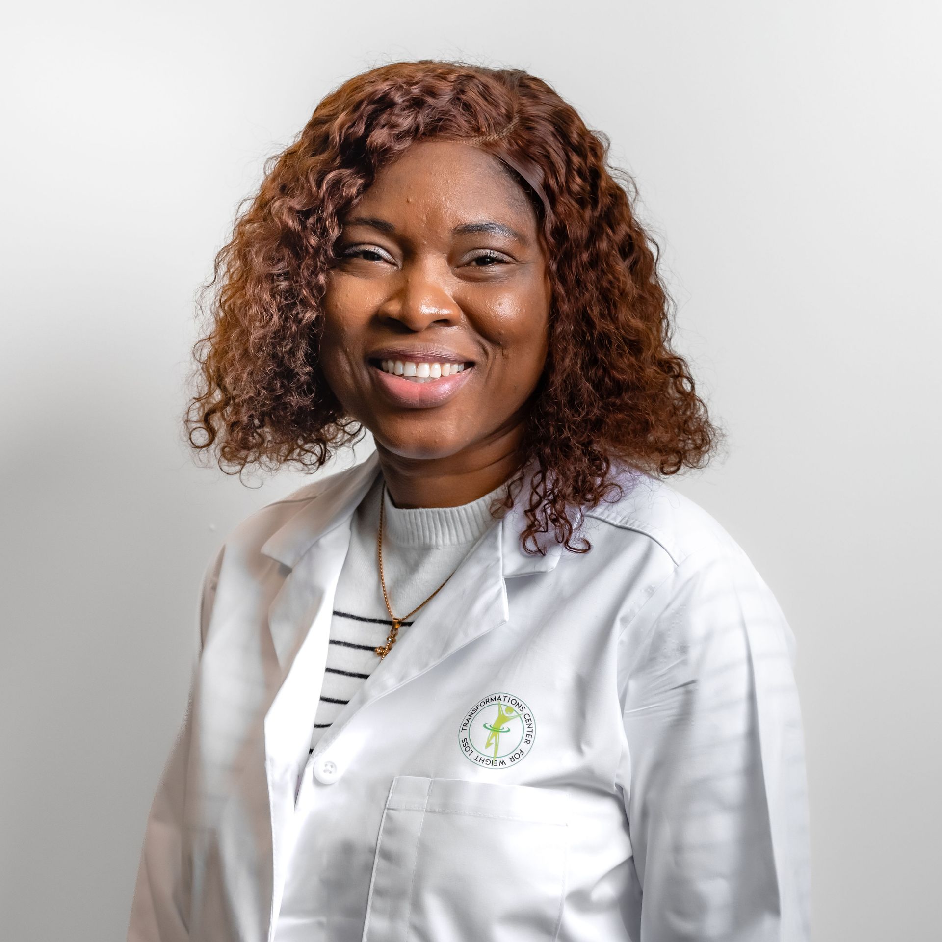 Woman in a white coat smiling, wearing a striped shirt and necklace.