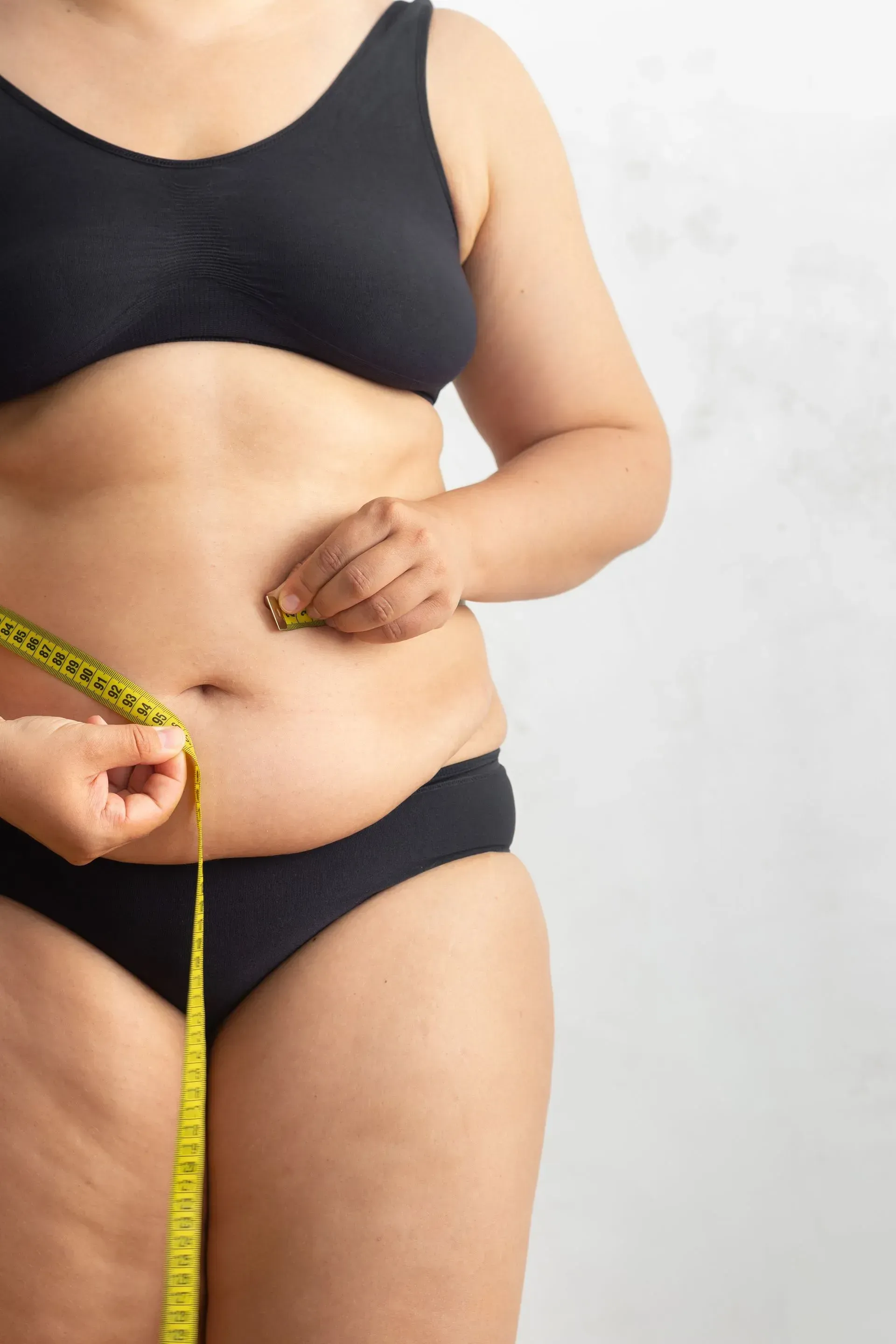 A woman is measuring her waist with a tape measure.