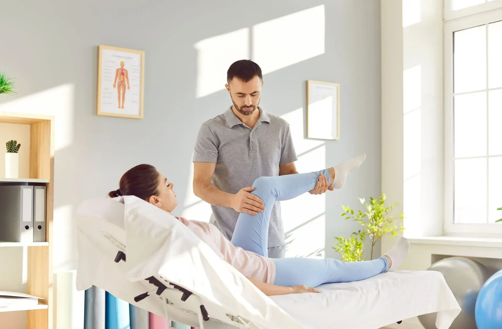 A man is helping a woman stretch her leg in a hospital bed.