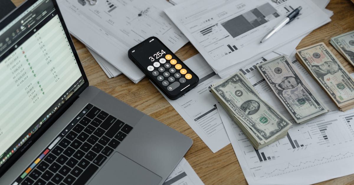 A laptop computer is sitting on a wooden table next to a pile of money and a calculator.