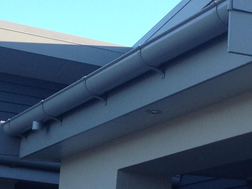 Gray gutter system on the edge of a building, attached to the fascia with metal brackets, under a blue sky.