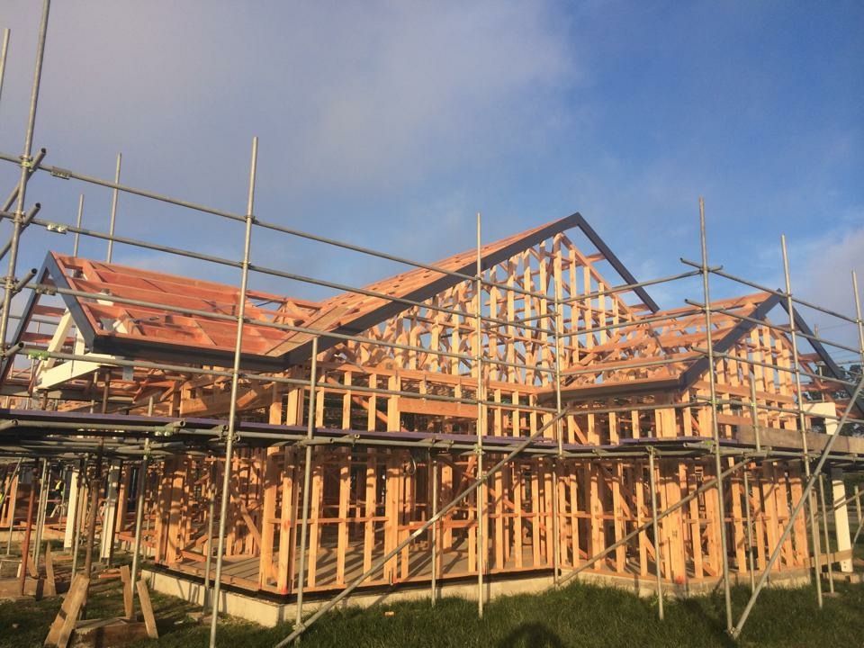 Wooden frame of a house under construction with scaffolding surrounding it, against a blue sky.