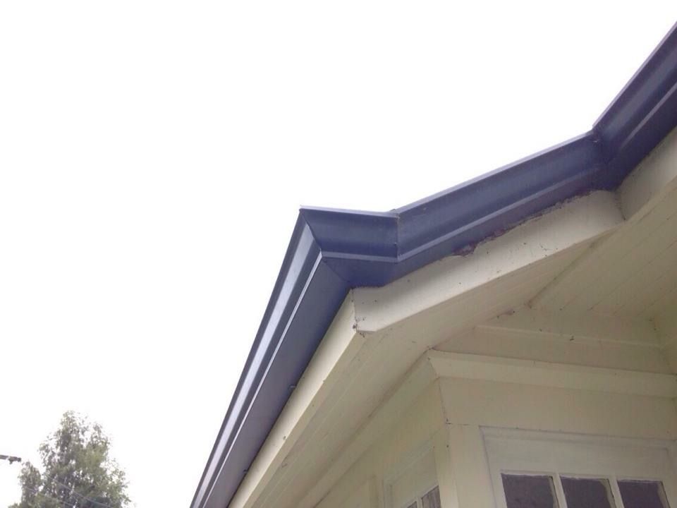 Dark gray rain gutter on a light yellow house. The sky is white and overcast.
