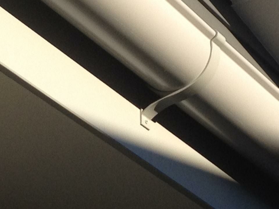White pipe held in place by a white metal bracket attached to a white surface, with shadows creating contrast.