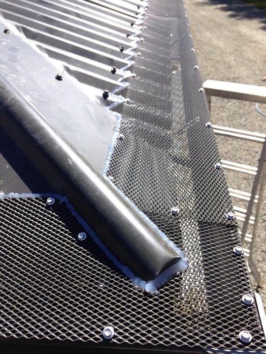 Black metal roofing with a gutter and protective mesh in a bright outdoor setting. The gutter is black and angled.