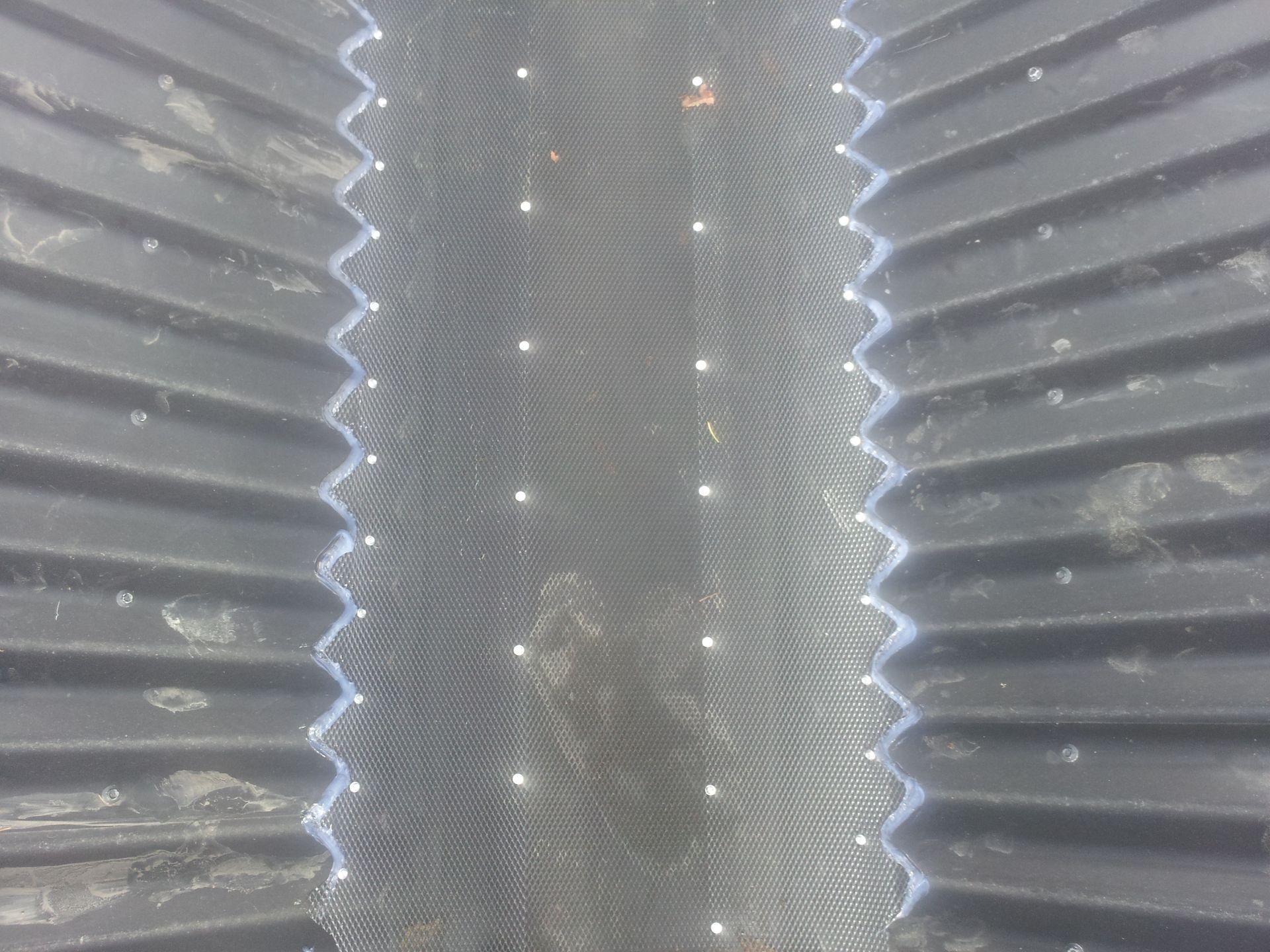 Close-up of a black corrugated structure with a central textured panel and a zigzag edge. Small white dots are visible.