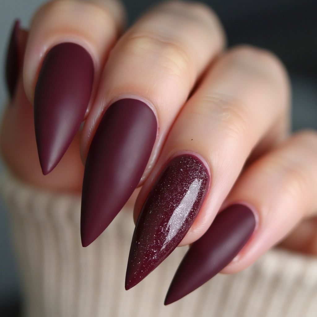 Hand with long, pointed, matte burgundy nails, one glittery.