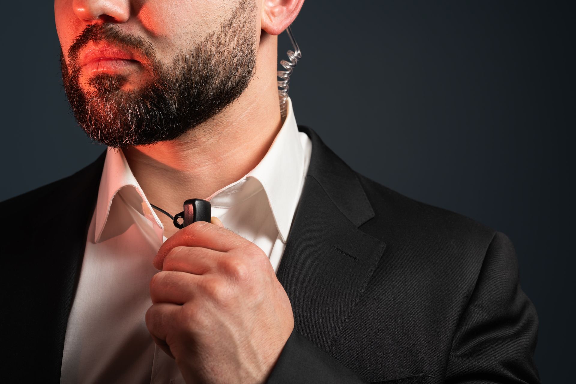 Man in black suit adjusting his tie under warm red light.