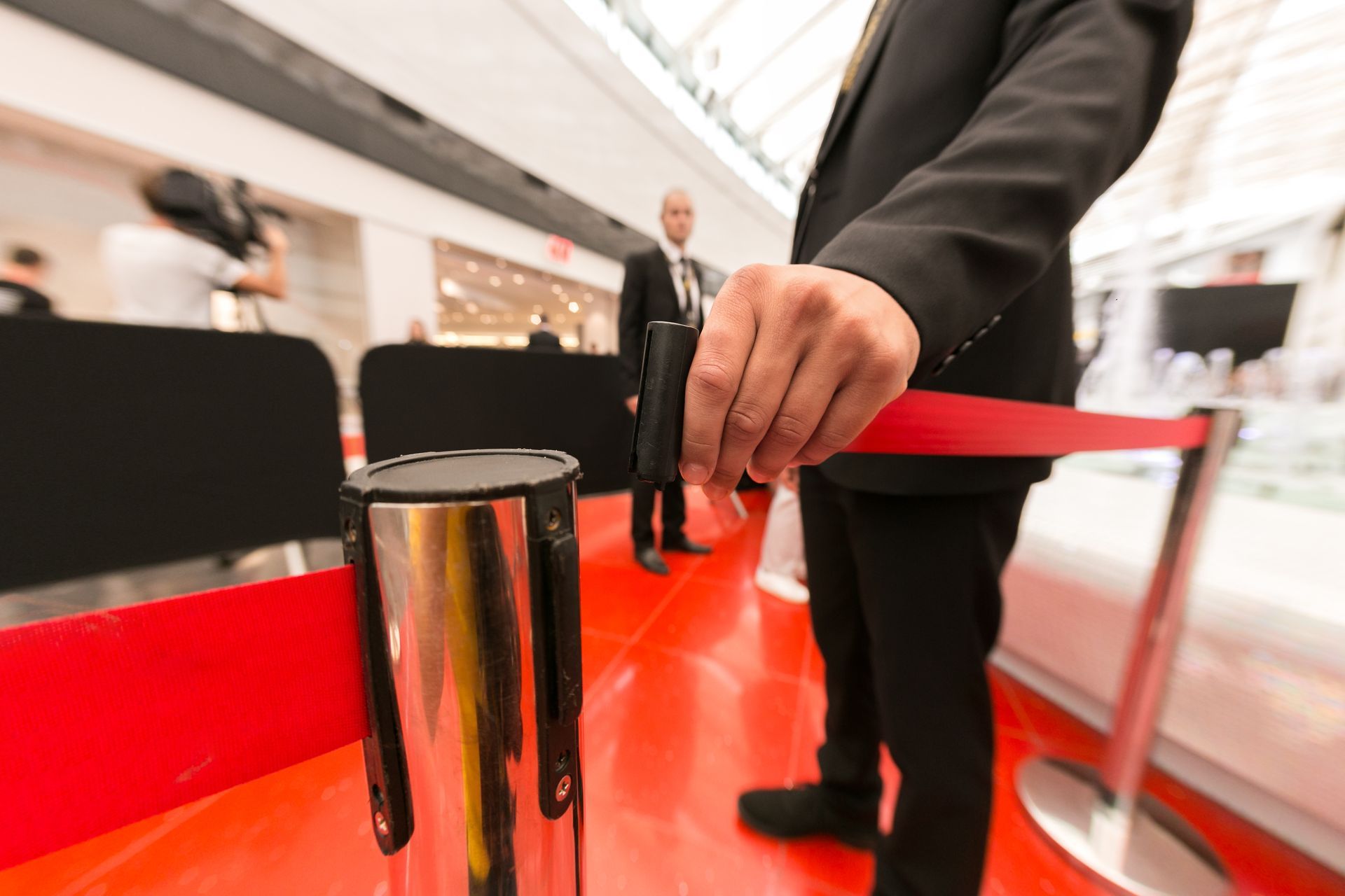 Person holding a red rope barrier at a glossy event entrance.