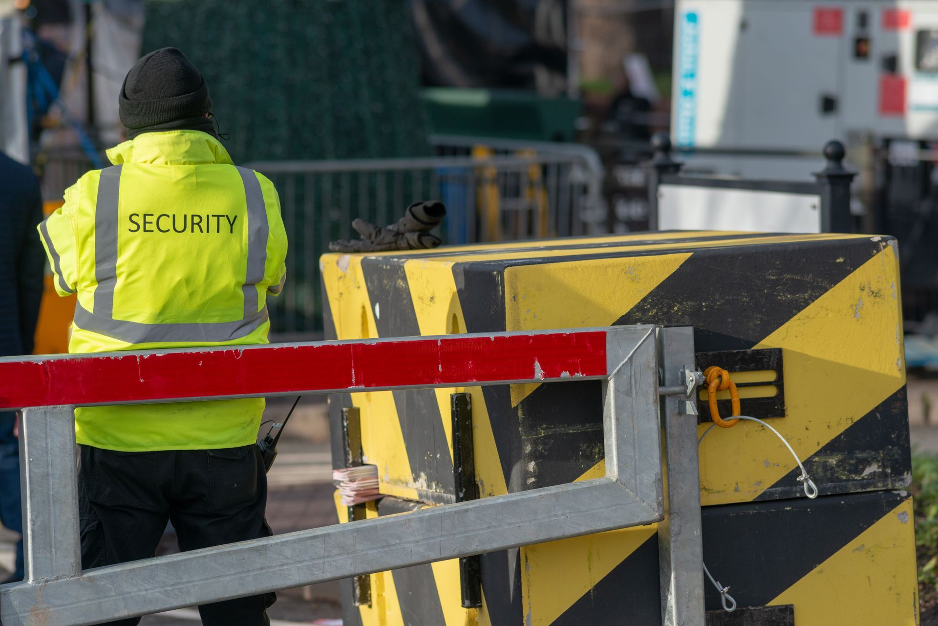 Security guard in neon yellow jacket beside a black-and-yellow barricade at a construction site.
