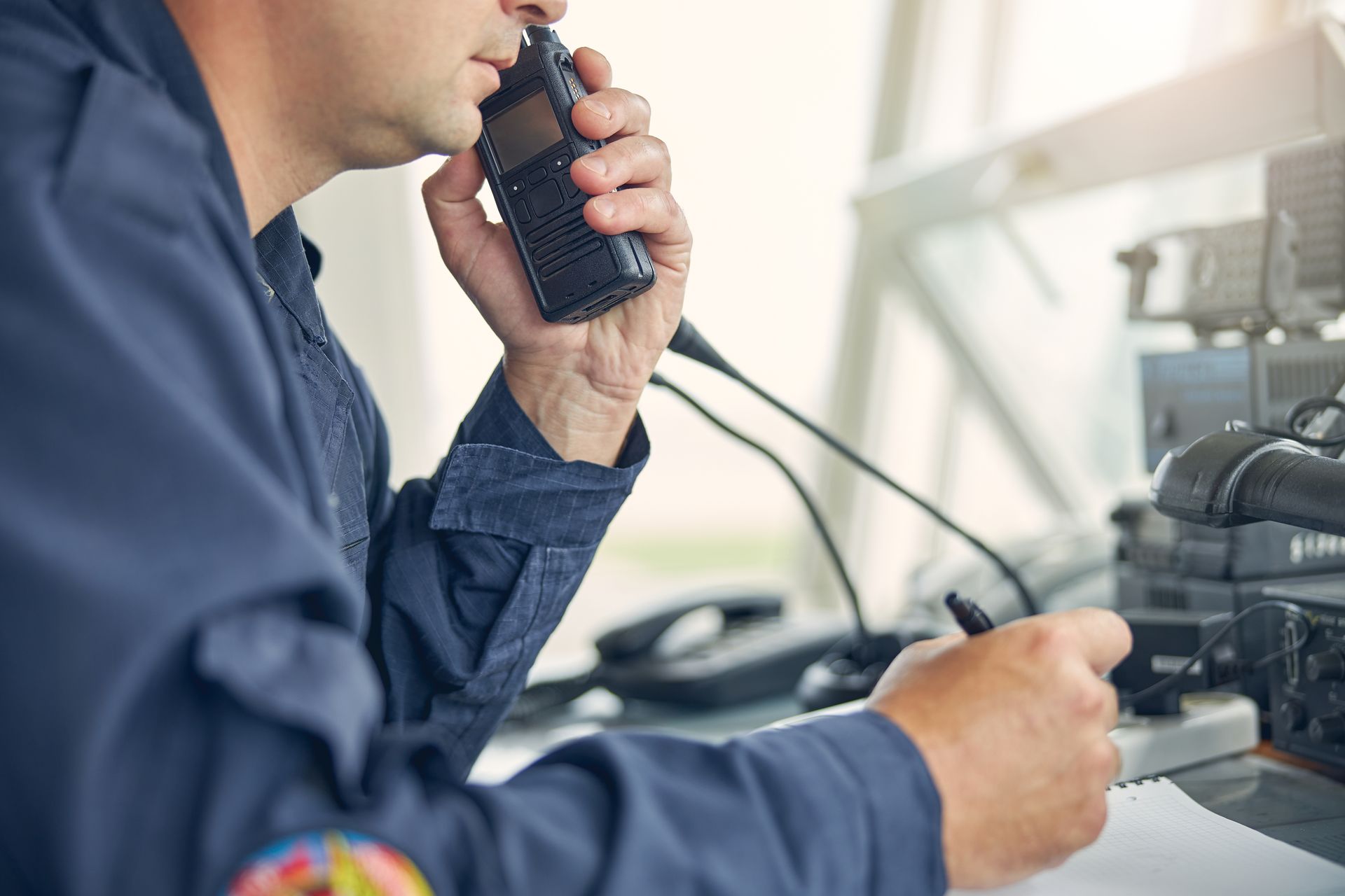 Person holding a walkie-talkie beside a radio control setup.