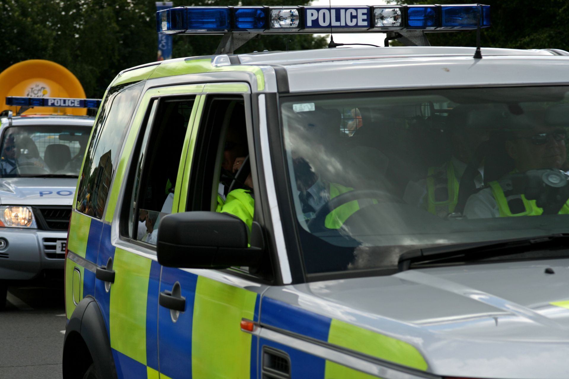Police car with blue lights parked on a street, with another vehicle behind it.