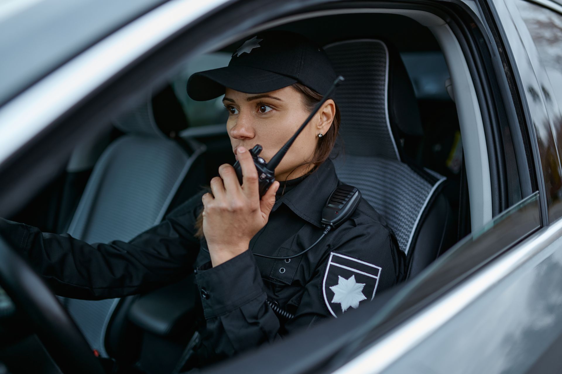 Uniformed security officer using a radio inside a vehicle.