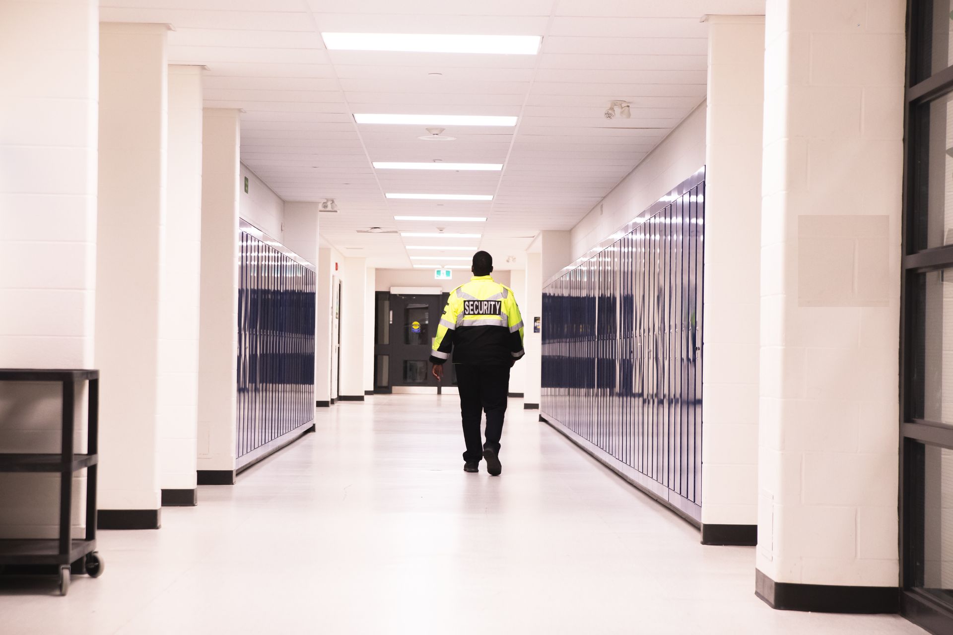 Person in a high-visibility jacket walking down a bright school hallway lined with lockers.